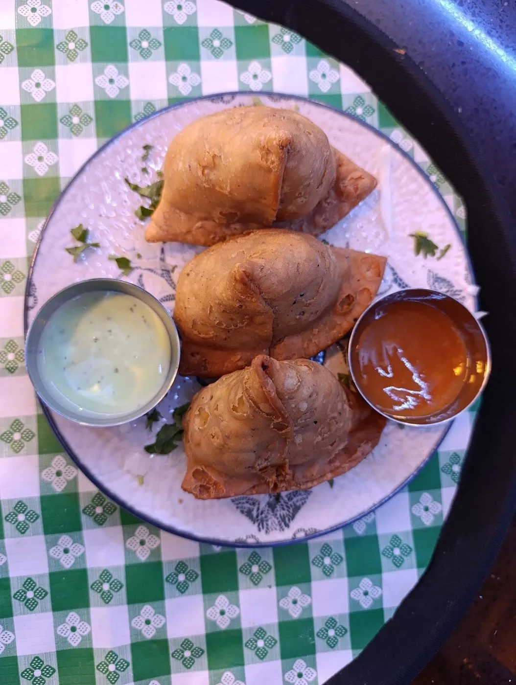 Tres samosas en un plato con dos salsas, sobre un mantel de cuadros verdes