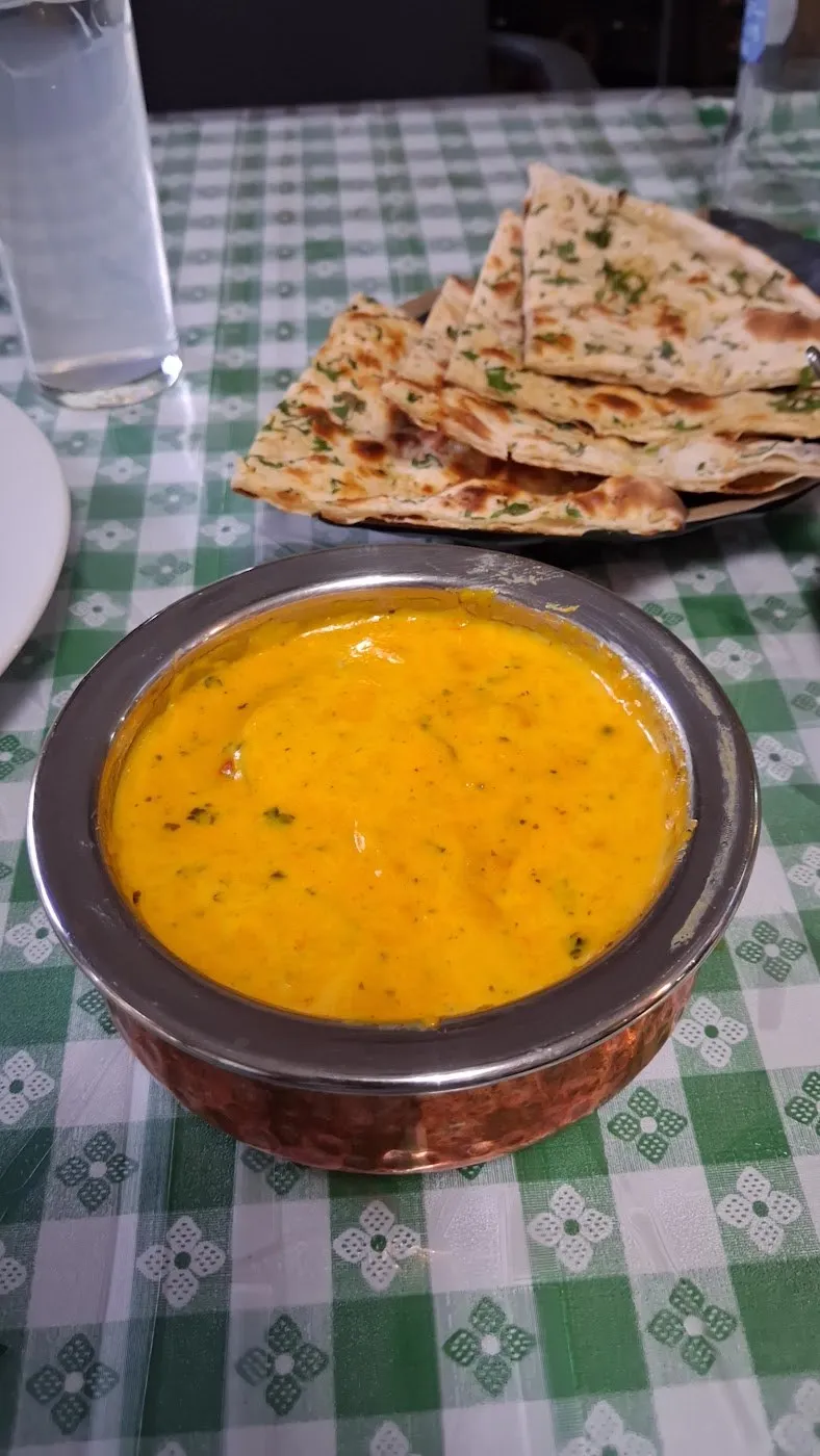 Curry amarillo en un cuenco de cobre con naan al fondo, sobre un mantel de cuadros verdes