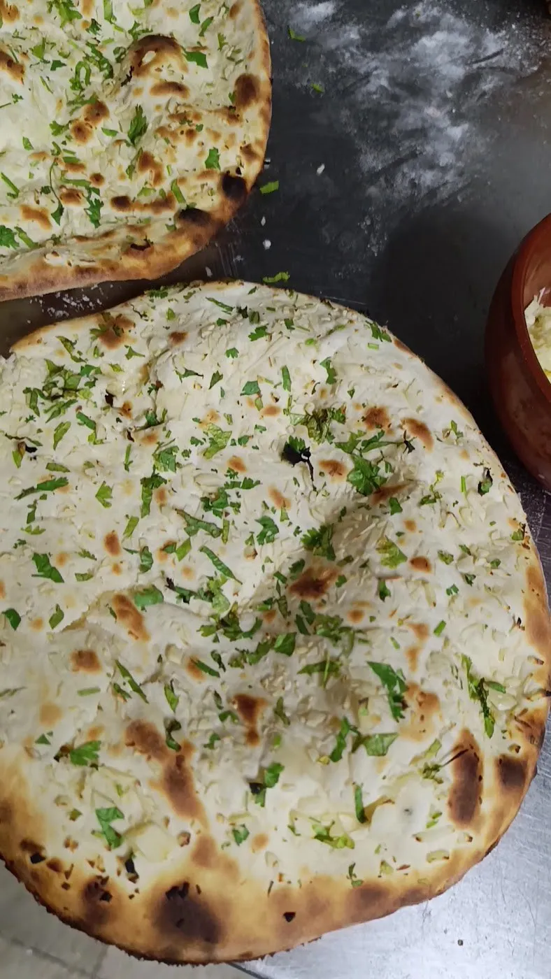 Naan con ajo y cilantro picado sobre una superficie oscura